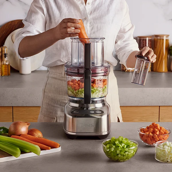 The Breville the Paradice 16 food processor sitting on a countertop while a woman puts celery and carrots into the chute to chop them