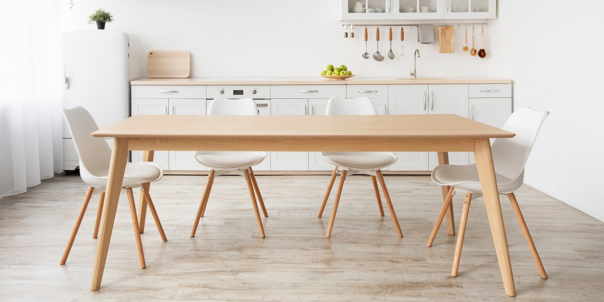 An image of an open-concept white small kitchen with a white dining/kitchen table in front of the room