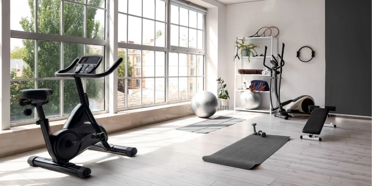 Modern home gym with exercise bike in the foreground and elliptical and exercise mats in the background.