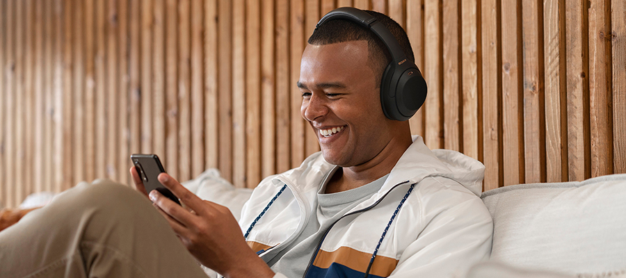 A man wearing black Sony over-ear headphones while he smiles and looks at his smartphone