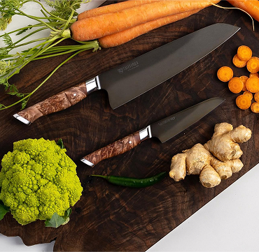 Overhead shot of two chef knives on a wooden cutting board situated around carrots, ginger and cauliflower
