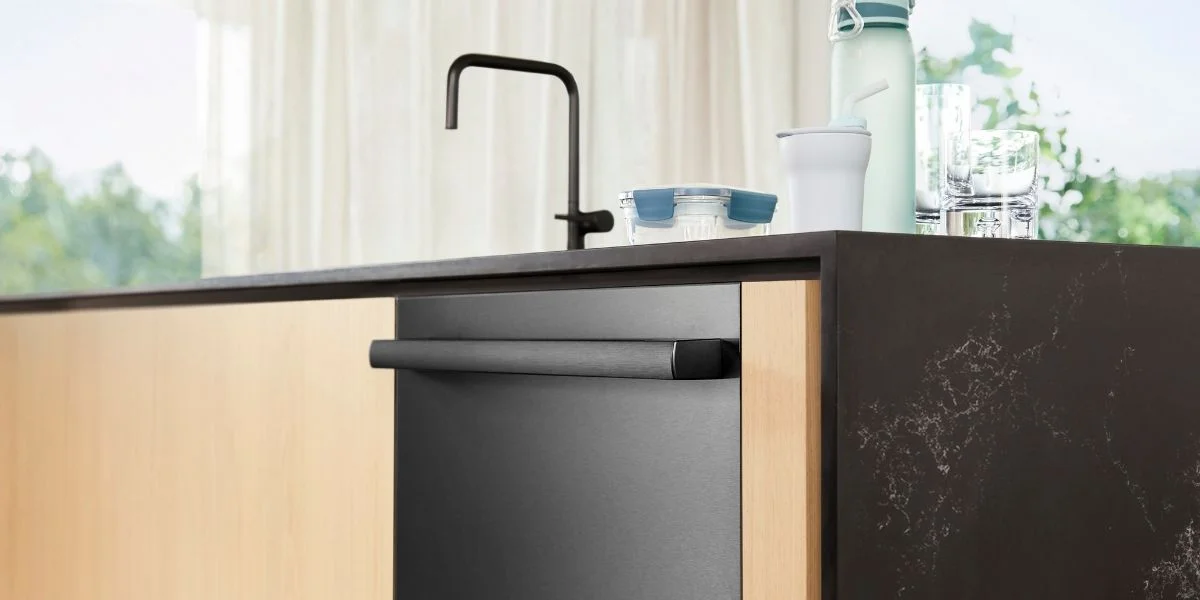 A zoomed in photo of a black stainless steel dishwasher built into a black stone kitchen island with light wood cabinetry.