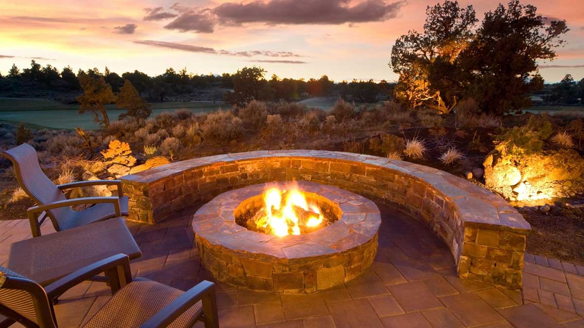 Stone fire pit surrounded by patio chairs as the sun sets