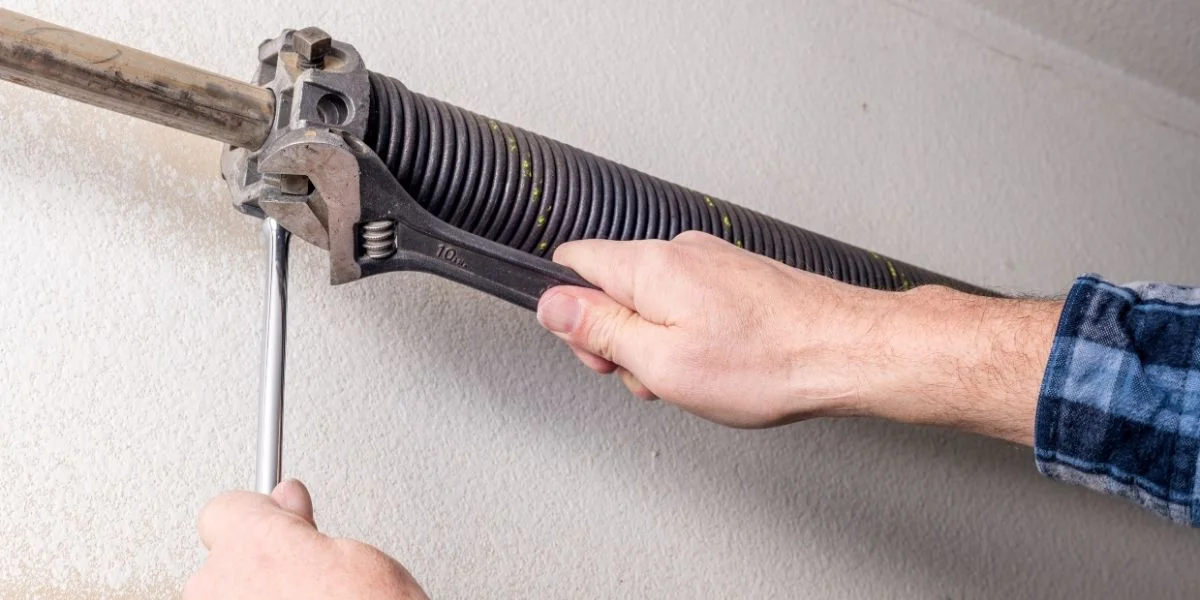 A man using a wrench to adjust a spring on a garage door wall