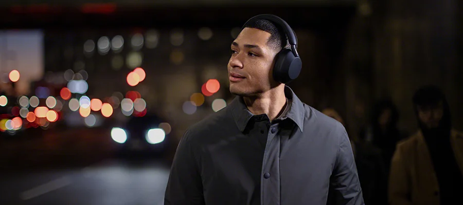 A man walking in the city at night wearing the Sony WH-1000XM5 headphones
