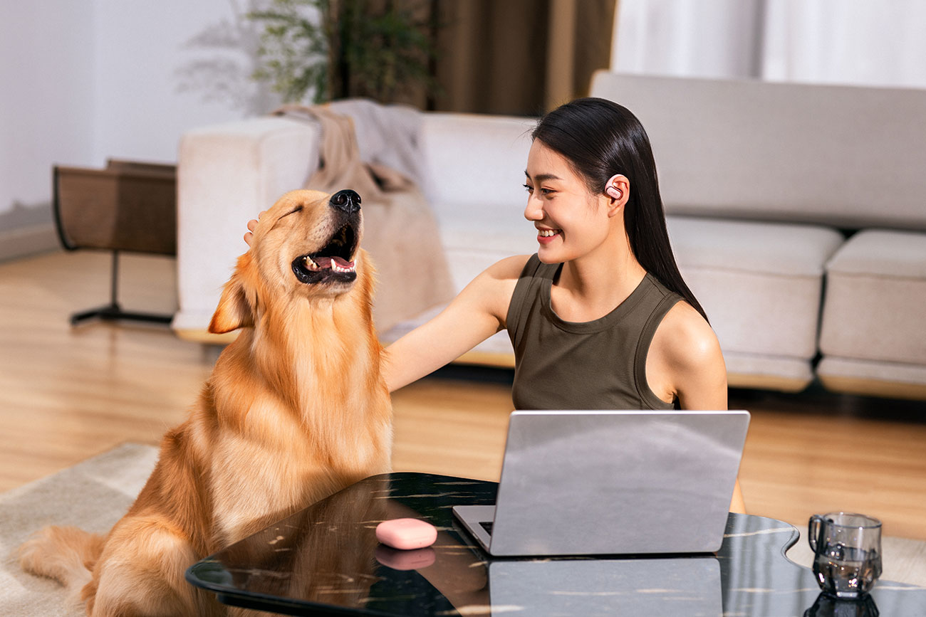 Woman Using Open-Ear Earbuds Indoors Next to a Dog
