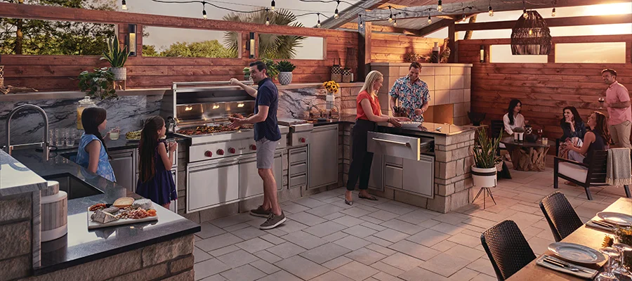 A group of family and friends hanging out, cooking and eating on a stone patio with a luxury outdoor kitchen.