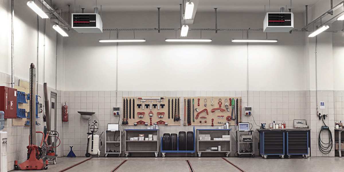 A garage with two reznor gas heaters hanging from the ceiling. Tools hang from the walls and sit along the walls