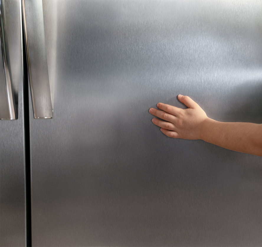A childs hand running across the stainless steel of a gallery refrigerator showing the smudge proof option