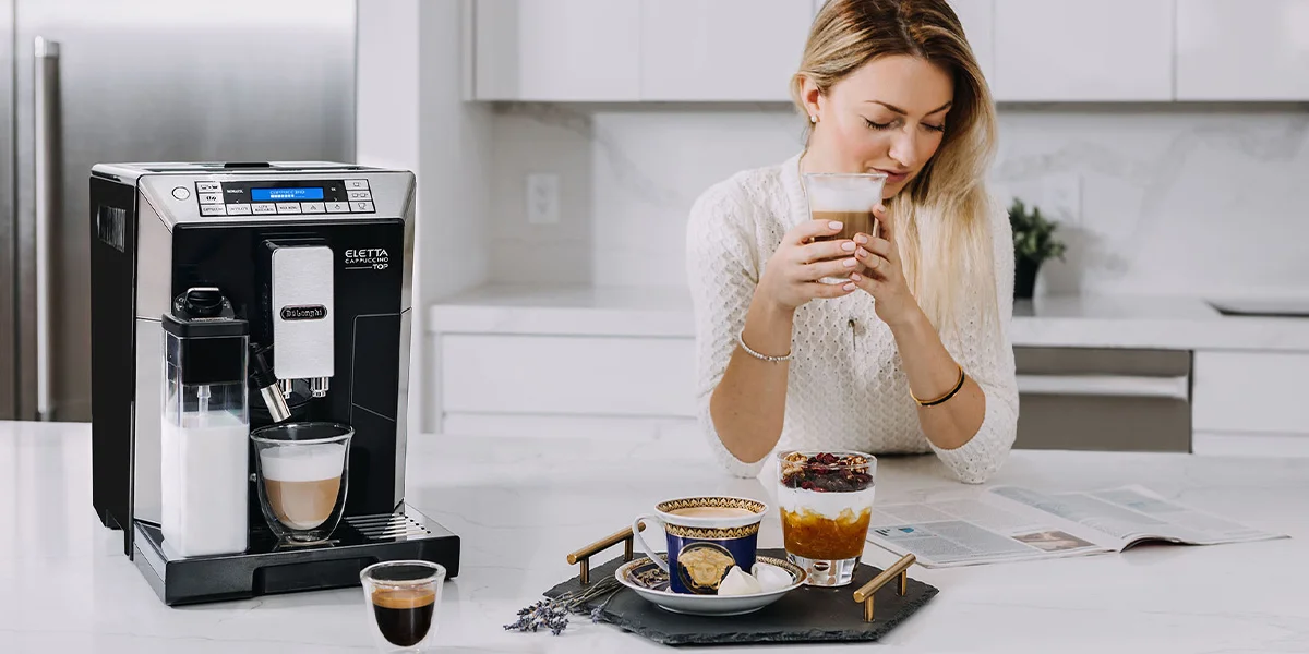 Woman reading a magazine while drinking espresso in the kitchen and espresso machine sitting on counter.