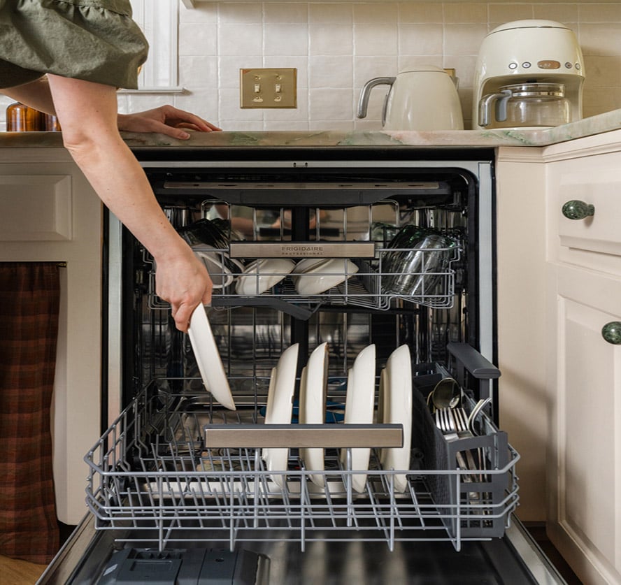 A person leaning from the countertop placing a plate in a frigidaire professional dishwasher
