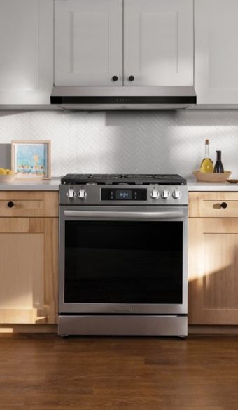 Tight shot on a built in stainless steel cooking range with a built in range hood above