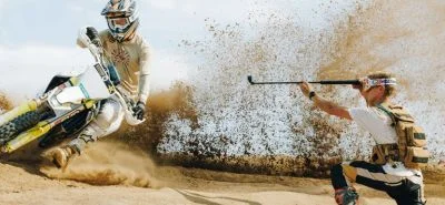 A man driving a dirt bike on the sand while being recorded by his friend with the HERO13 on a mount.