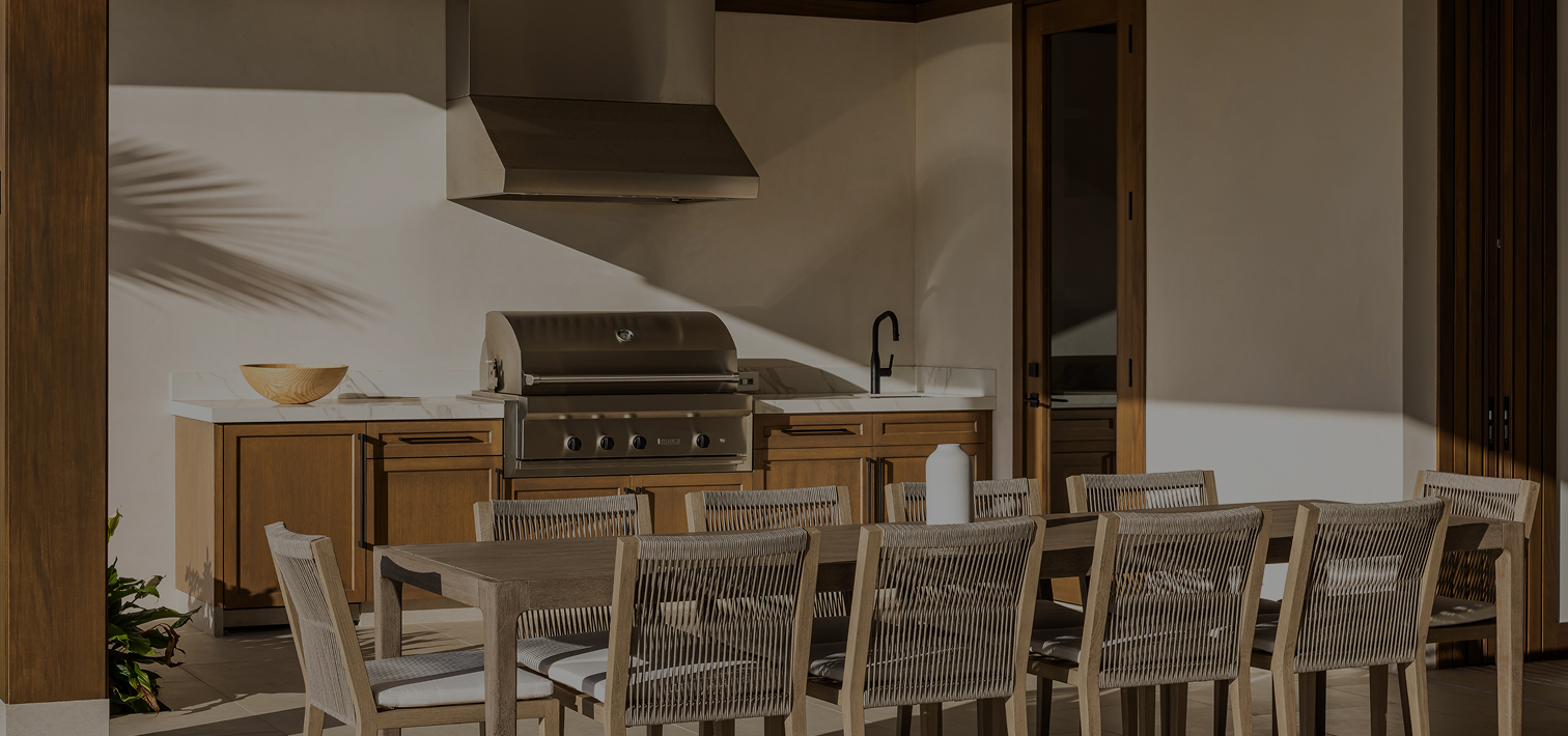 A stylish outdoor patio fitted with a built-in wolf grill and hood in the background and a modern outdoor dining table 10 chairs arranged around it