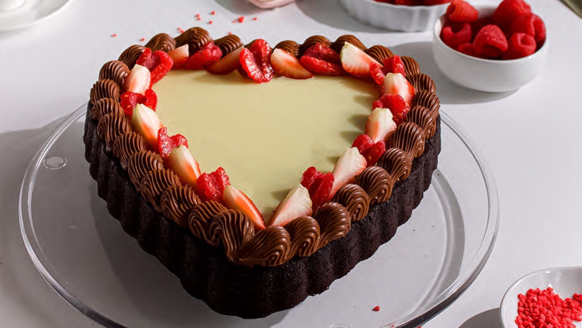 heart-shaped chocolate cake with strawberries on top sitting on glass plate