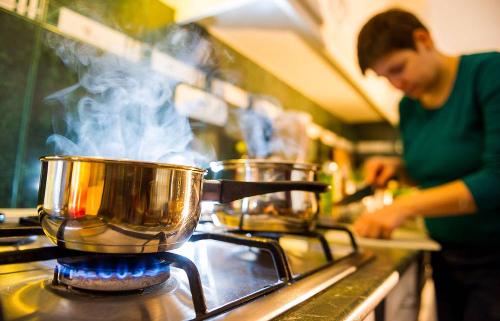 Person cooking near two pots on a gas stove top