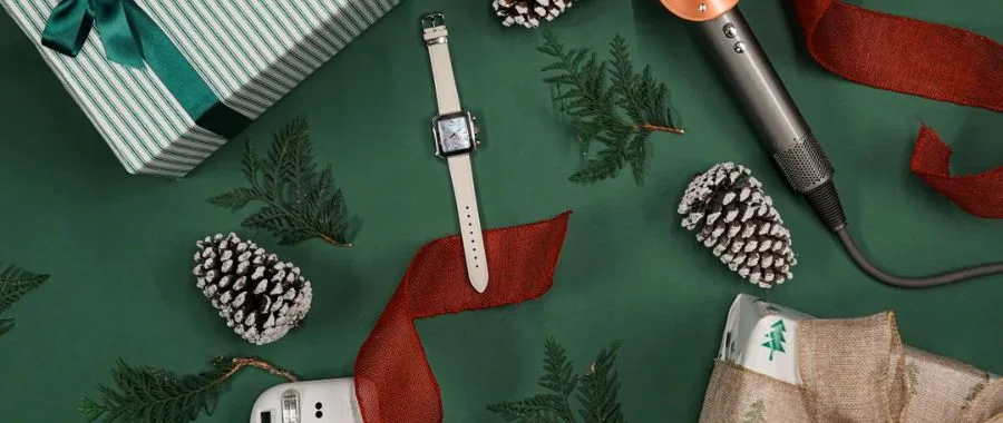 a watch, wrapped gift and other holiday presents on a green background