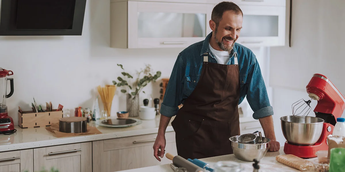 A man wearing an apron beside his stand mixer in the kitchen, mixing doughs and baking.
