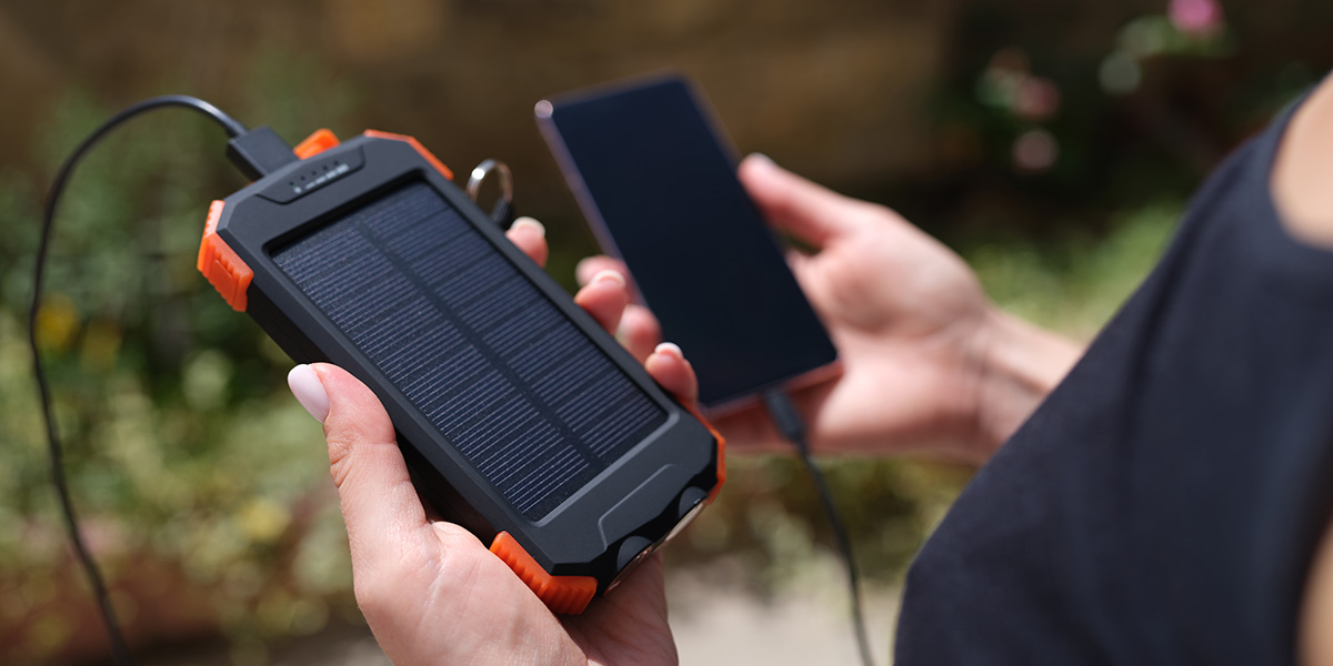 A person charging their phone outdoors using what looks like a solar-powered portable power bank