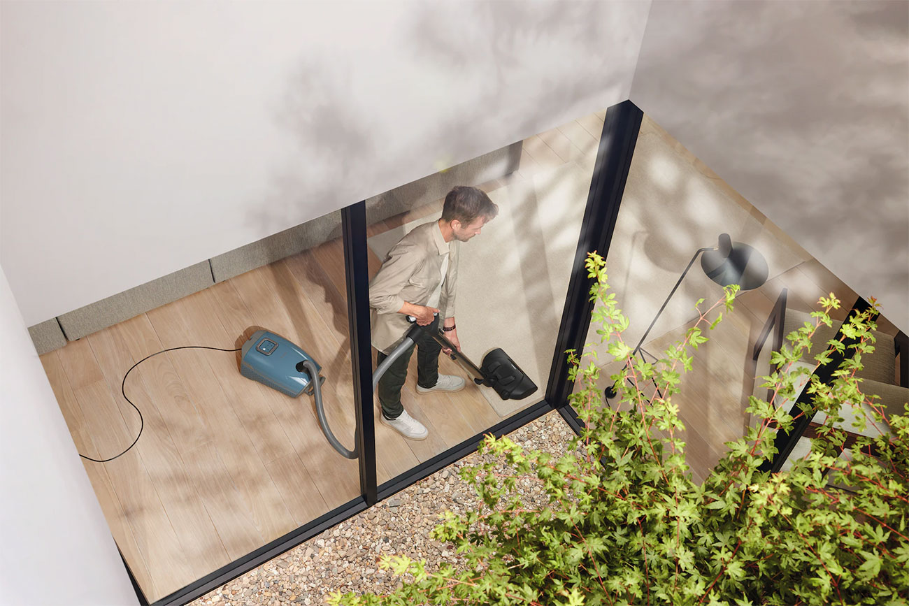 Front View of Man Using the Miele Cannister Vacuum In Living Room