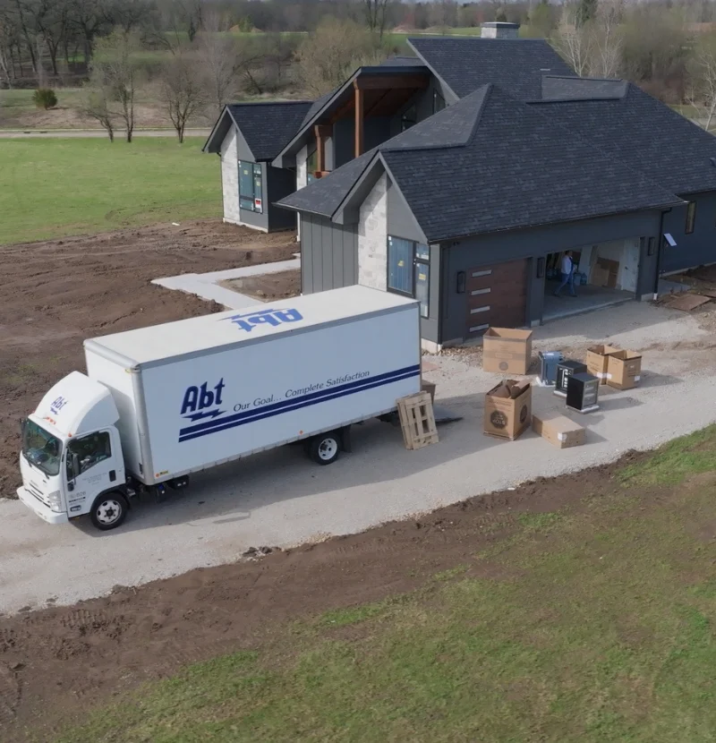 An Abt truck parked outside of a house with unloaded boxes of appliances.
