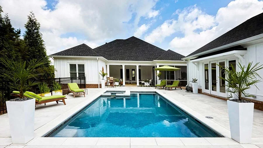 Rectangular pool with green chaise lounges and patio umbrella on the surrounding deck.
