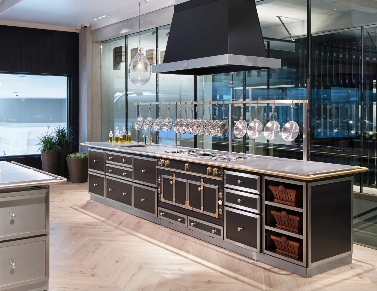 La Cornue showroom kitchen island with a black range, hanging cookware and glass walls