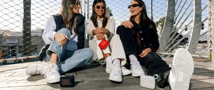 Three girls sitting outside, each with their own JBL Go 4