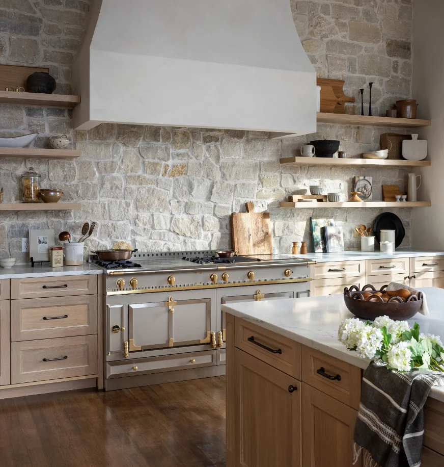 Taupe La Cornue range in a kitchen with a stacked stone accent wall and open wood shelving