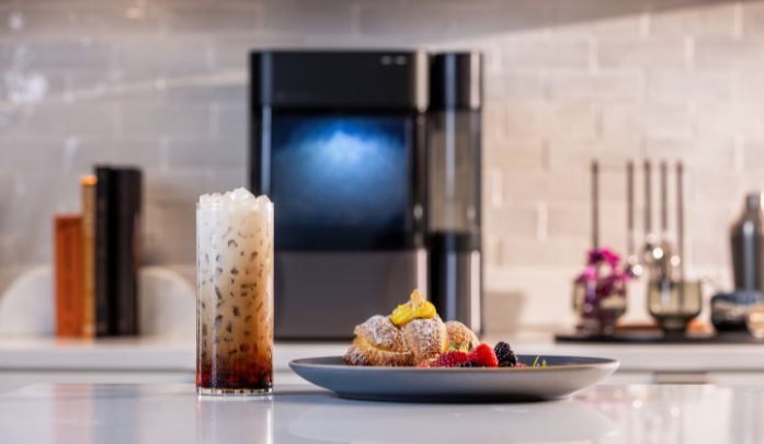 Ge profile countertop ice maker out of focus in the background with an iced coffee and the ice from the nugget ice maker and a pastry