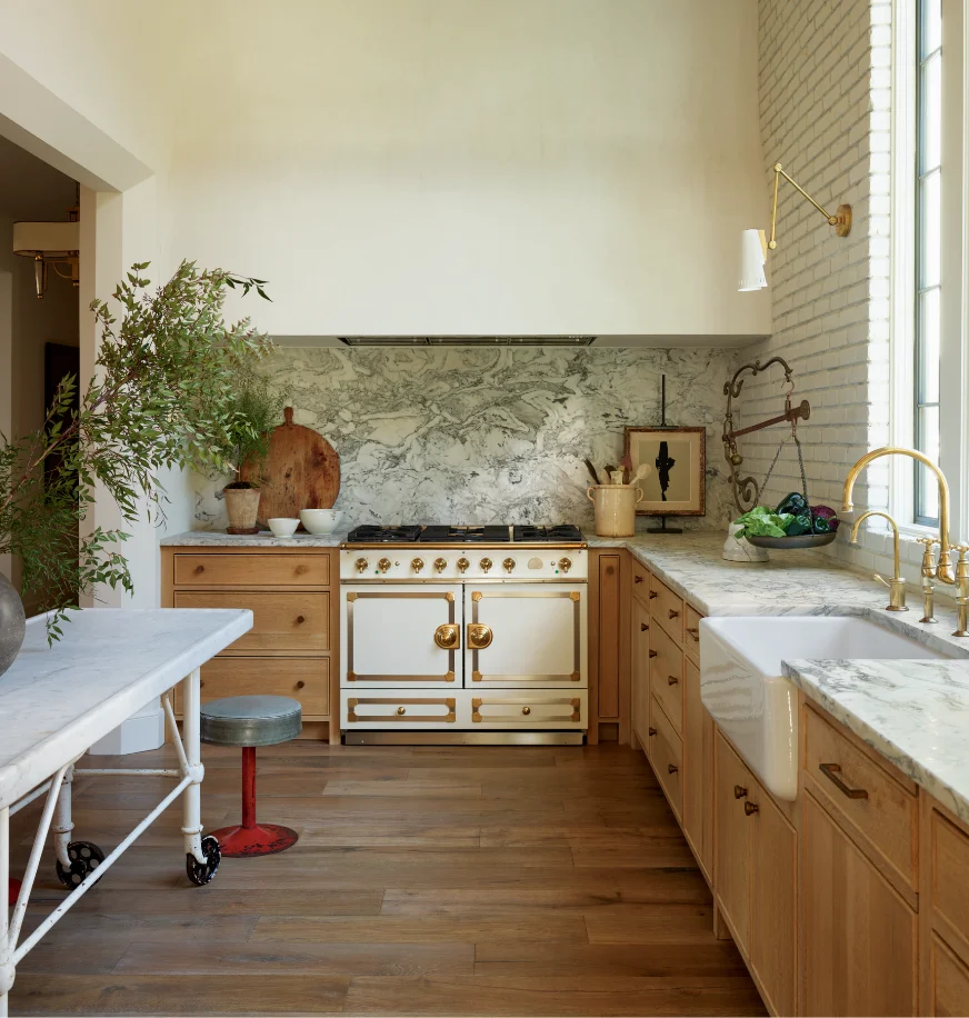 Cream La Cornue range with brass trim in a kitchen with marble backsplash and a farmhouse sink