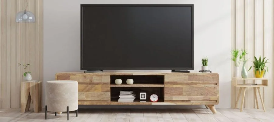 A TV on a TV stand in a living room. The aesthetic in the room is neutral with small plants nearby