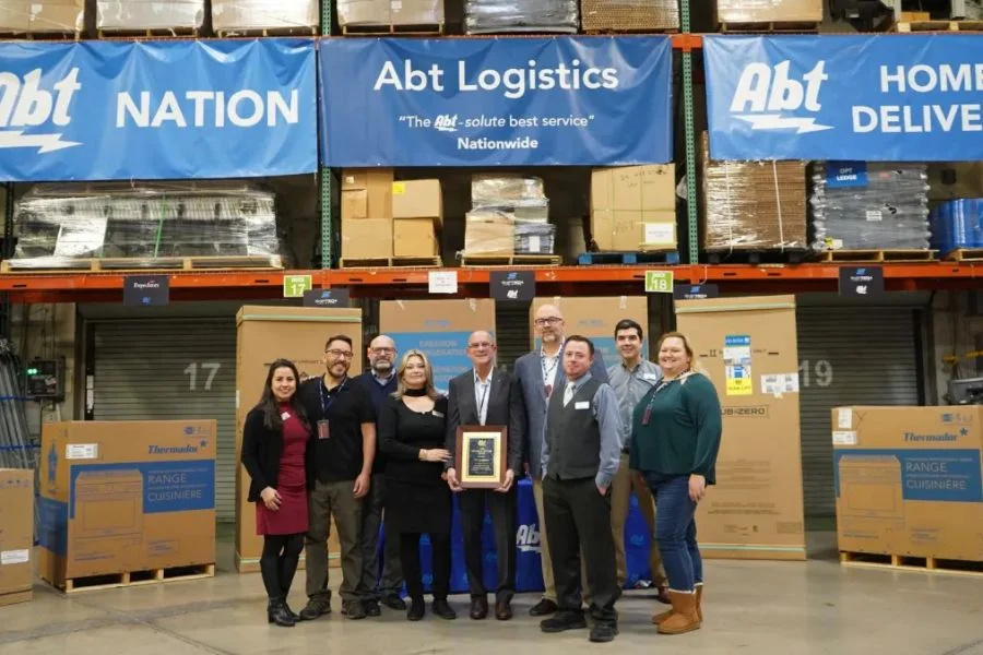 TCA & Abt Logistics team members together with signs overhead that read "Abt Nation. Abt Logistics, and Abt Home Delivery"