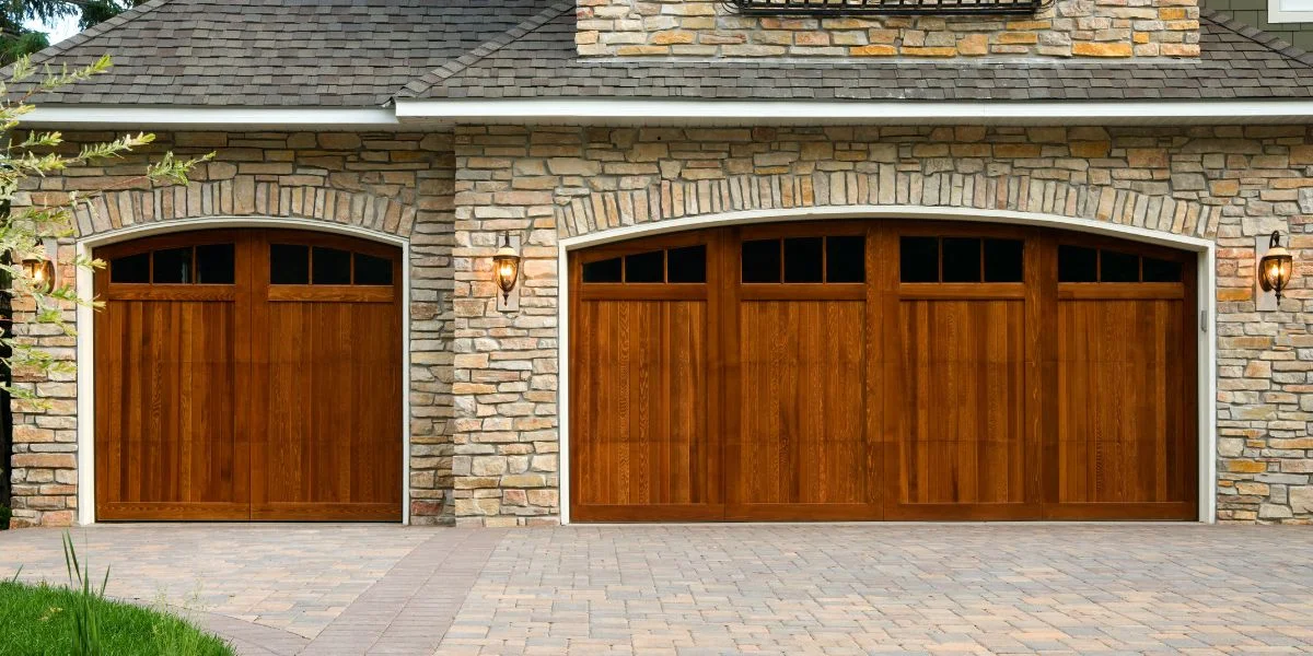 A single garage door next to a double garage door, each is a deep brown with curved windows along the top.