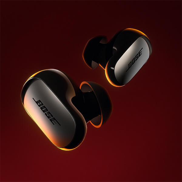 A pair of black Bose earbuds in front of a solid red background