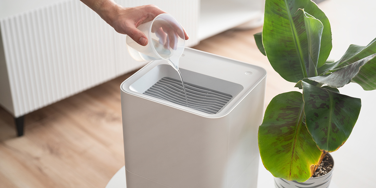 A hand pouring a clear cleaning solution into a white humidifier