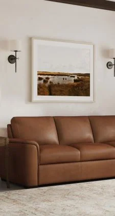 tight shot on a brown leather couch in a modern living room setting sitting in front of a western like picture and two light fixtures to the right and left of the picture
