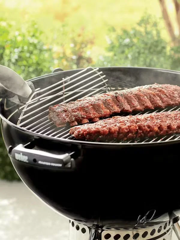 A close shot on a weber charcoal grill with ribs situated on the grill grates