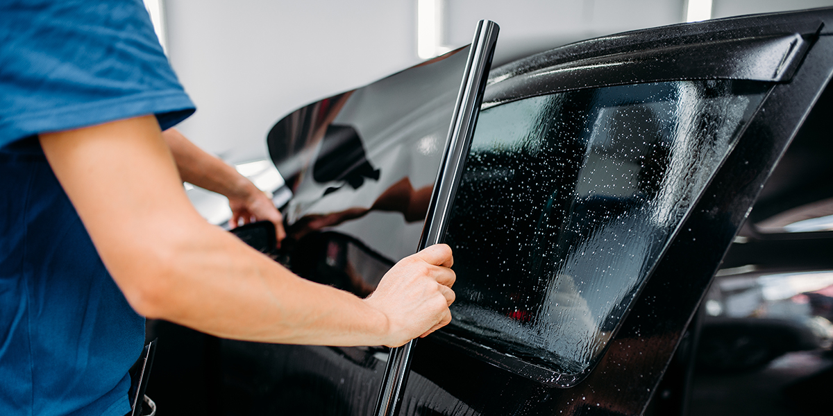 A technician applying black widow film to a vehicle with a damp window