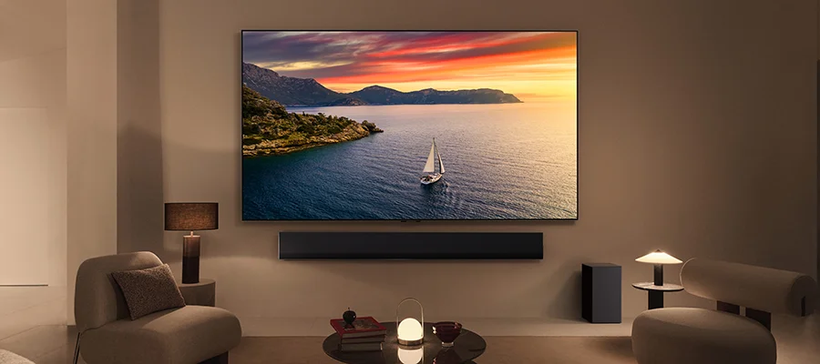 The LG G4 TV mounted on the wall of a beige living room displaying an image of a sailboat on the water at sunset