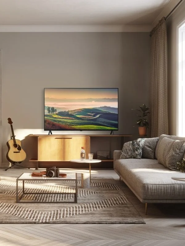 OLED TV in a living room modern living room setting with a couch, rug, coffee table and a guitar aside the tv