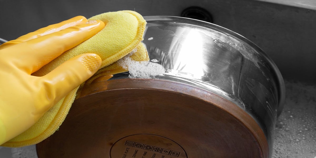 Gloved hand washing stainless steel pot with a sponge