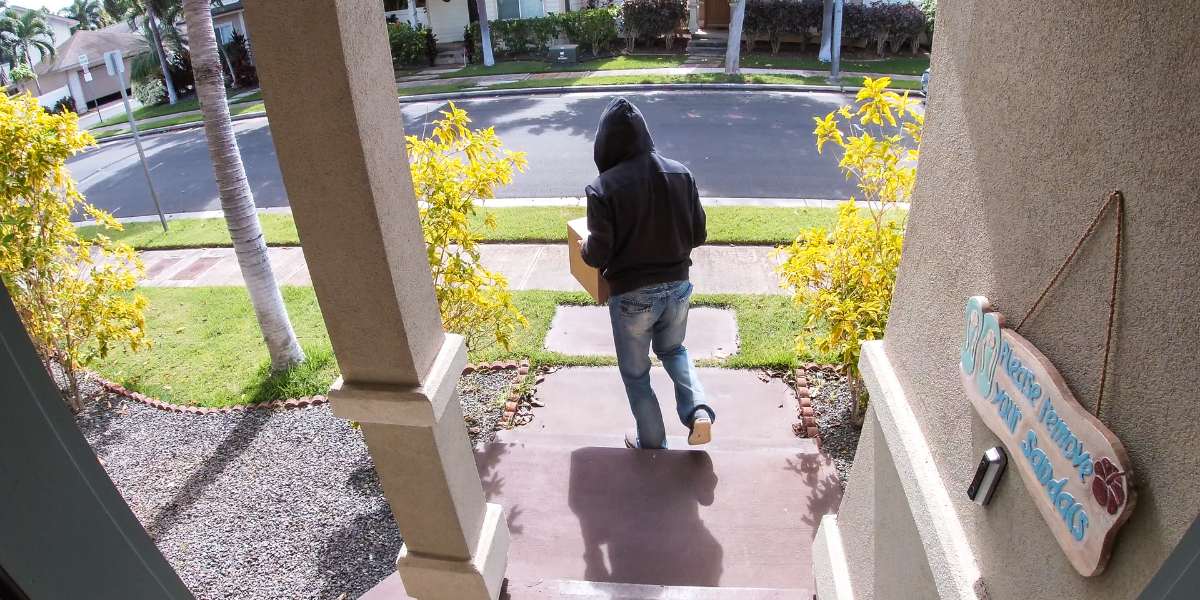 A man stealing a package from a front door and walking away on camera