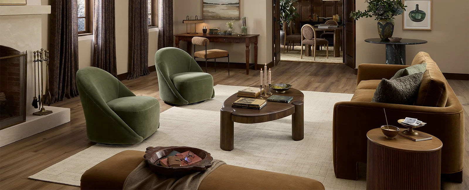 Spacious, stylish living room with a brown sofa, two green swivel lounge chairs, a wood coffee table on a light area rug, decorative wall art and plants, and an arched entryway leading to a dining space.