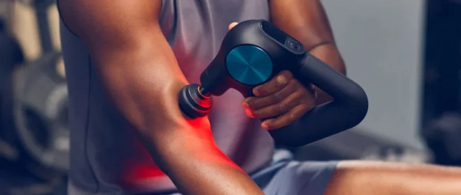 A man using a Therabody Theragun Pro on his arm muscles in a fitness center