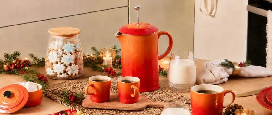 Le Creuset French press coffee maker in Flame on a kitchen table surrounded by coffee cups and holiday decor,