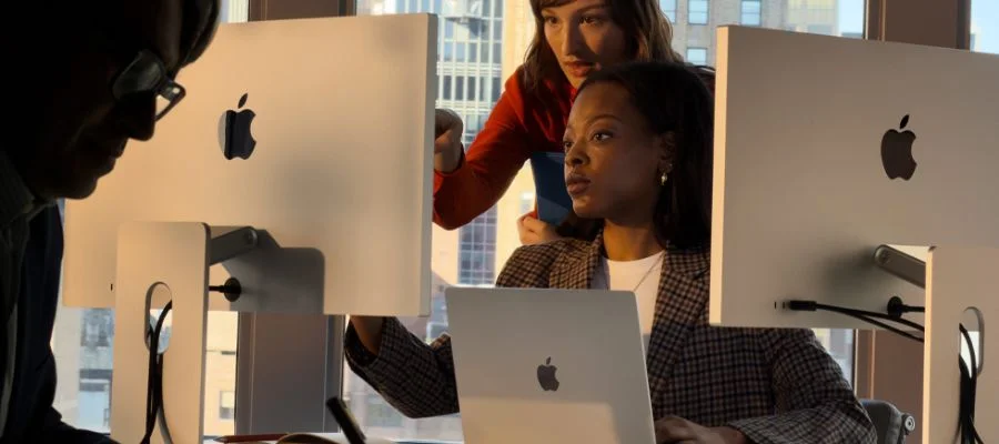 Two women using a MacBook and two Mac Studio displays in an office.