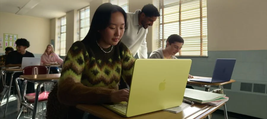 A student in a classroom using a MacBook Neo in Citrus. Other students behind her are using other MacBook Neo laptops.