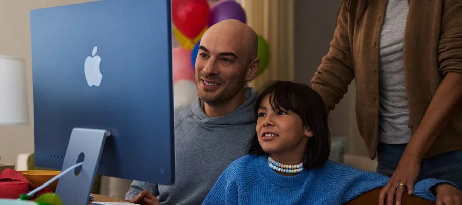 A mother, father and child looking at a blue iMac together.