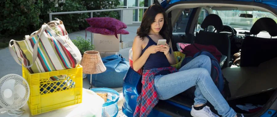 A college student preparing to leave for college. Her things are gathered around the truck of her car.